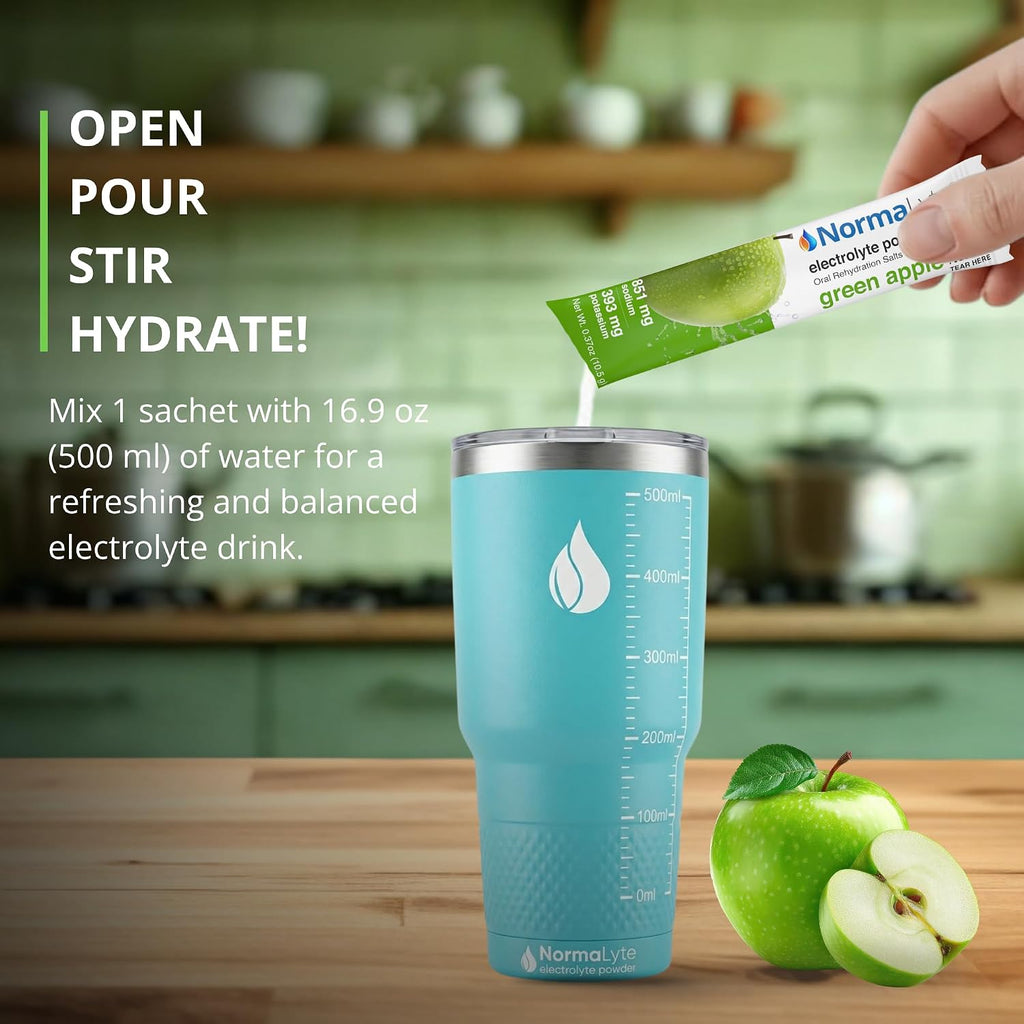 A light blue insulated tumbler with measurement markings sits on a wooden countertop in a blurred kitchen setting. A hand is pouring a green electrolyte packet into the tumbler, with a green apple beside it and promotional text on the left.