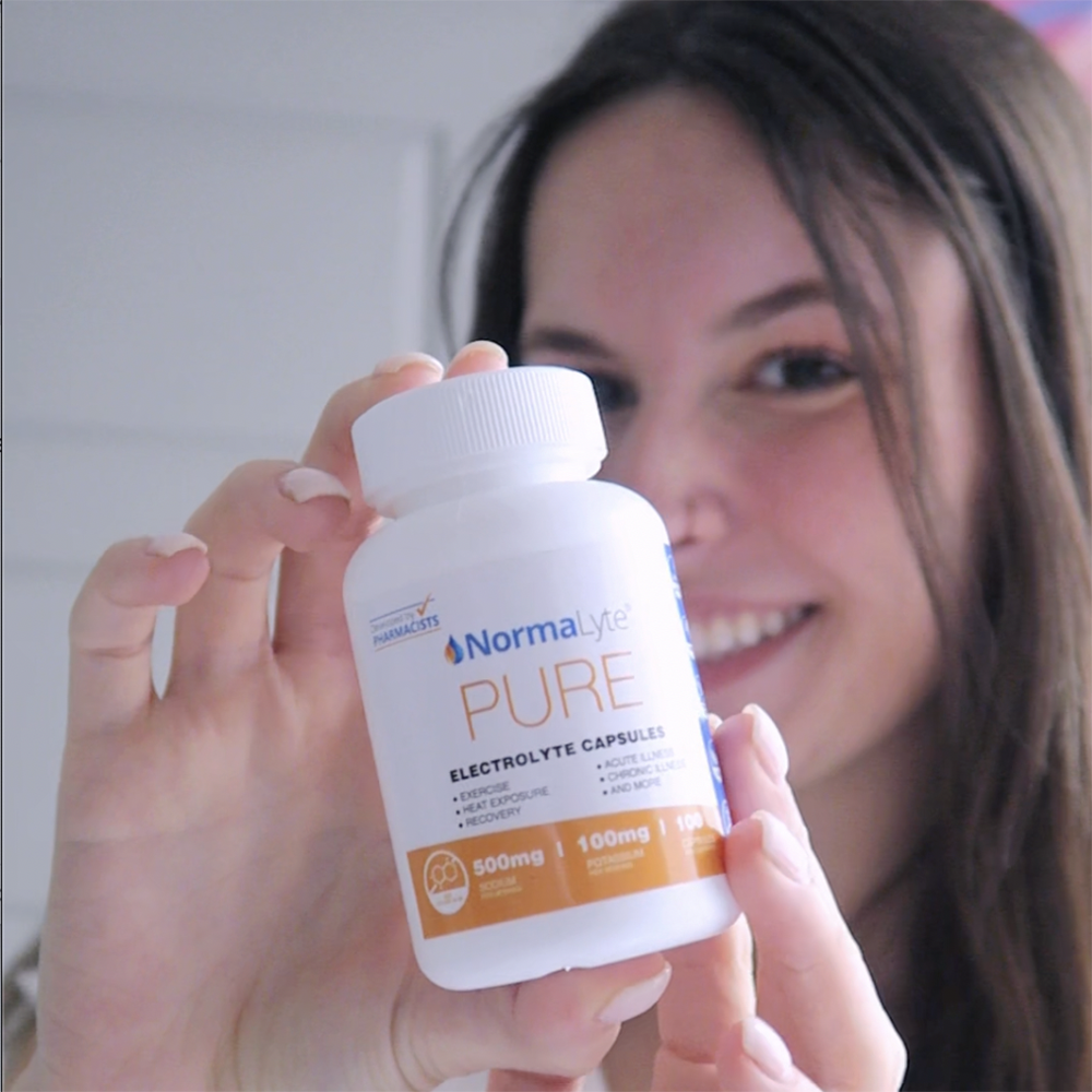 A very happy woman holding a bottle of NormaLyte Electrolyte Salt Capsules out in front of her face.