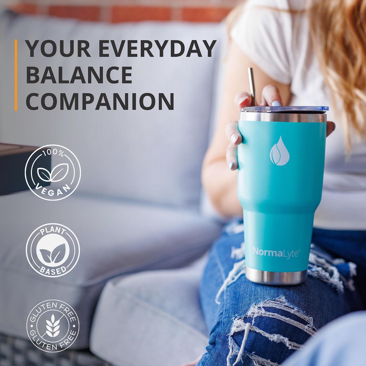 A person sitting on a couch holds a turquoise insulated tumbler with a clear lid and metal straw. Large text reads 'YOUR EVERYDAY BALANCE COMPANION,' with circular badges noting 100% vegan, plant-based, and gluten free.