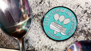 Salty and low on spoons NormaLyte pin sitting on top of sea salt with spoons surrounding it