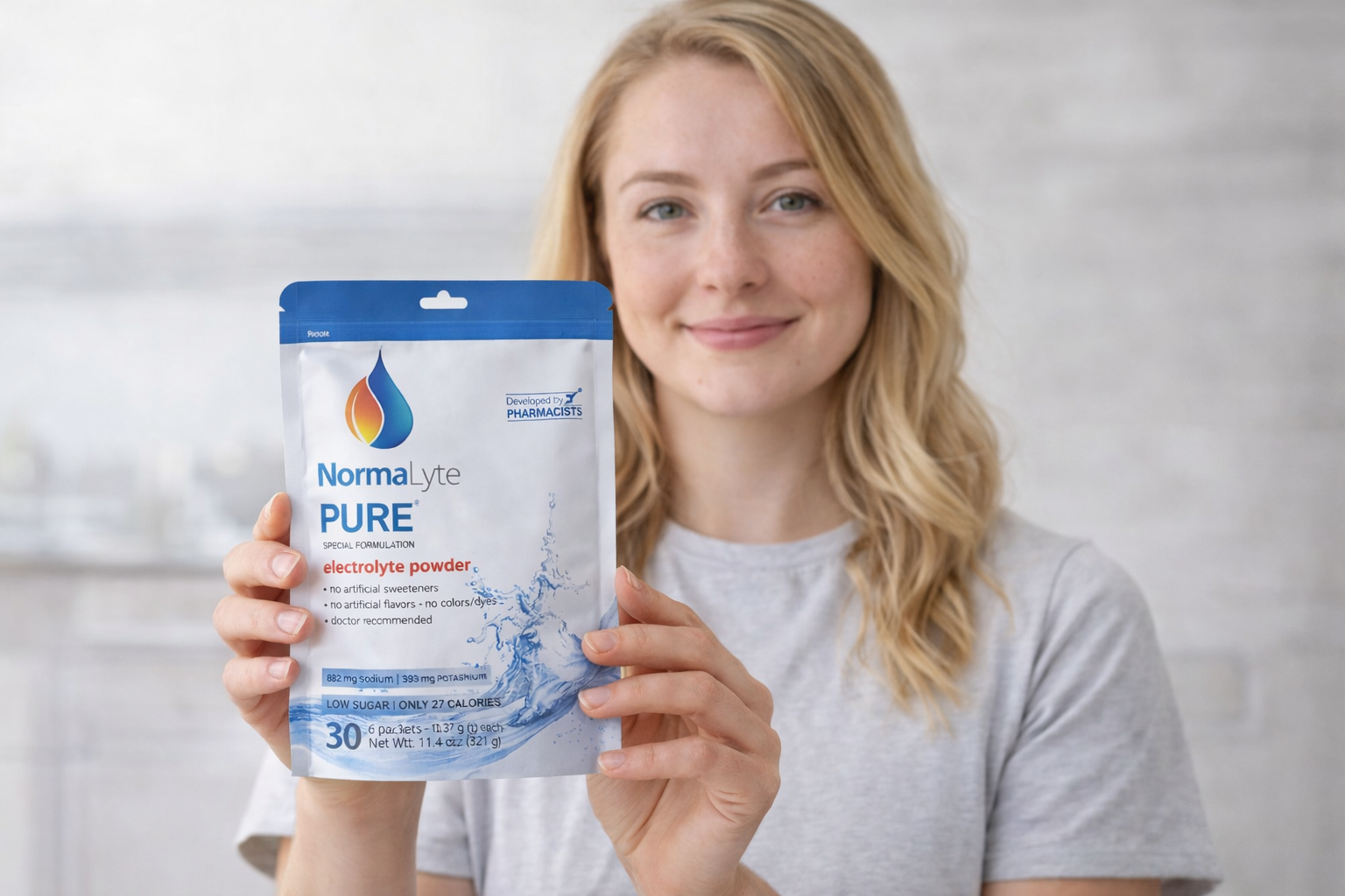 Woman holding a pouch of NormaLyte PURE electrolyte powder, a low-sugar formula developed by pharmacists.