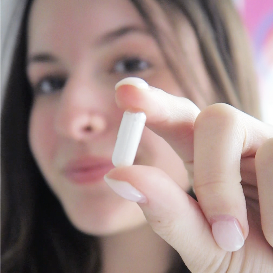 Close-up of a person holding a single white NormaLyte PURE electrolyte capsule between two fingers.