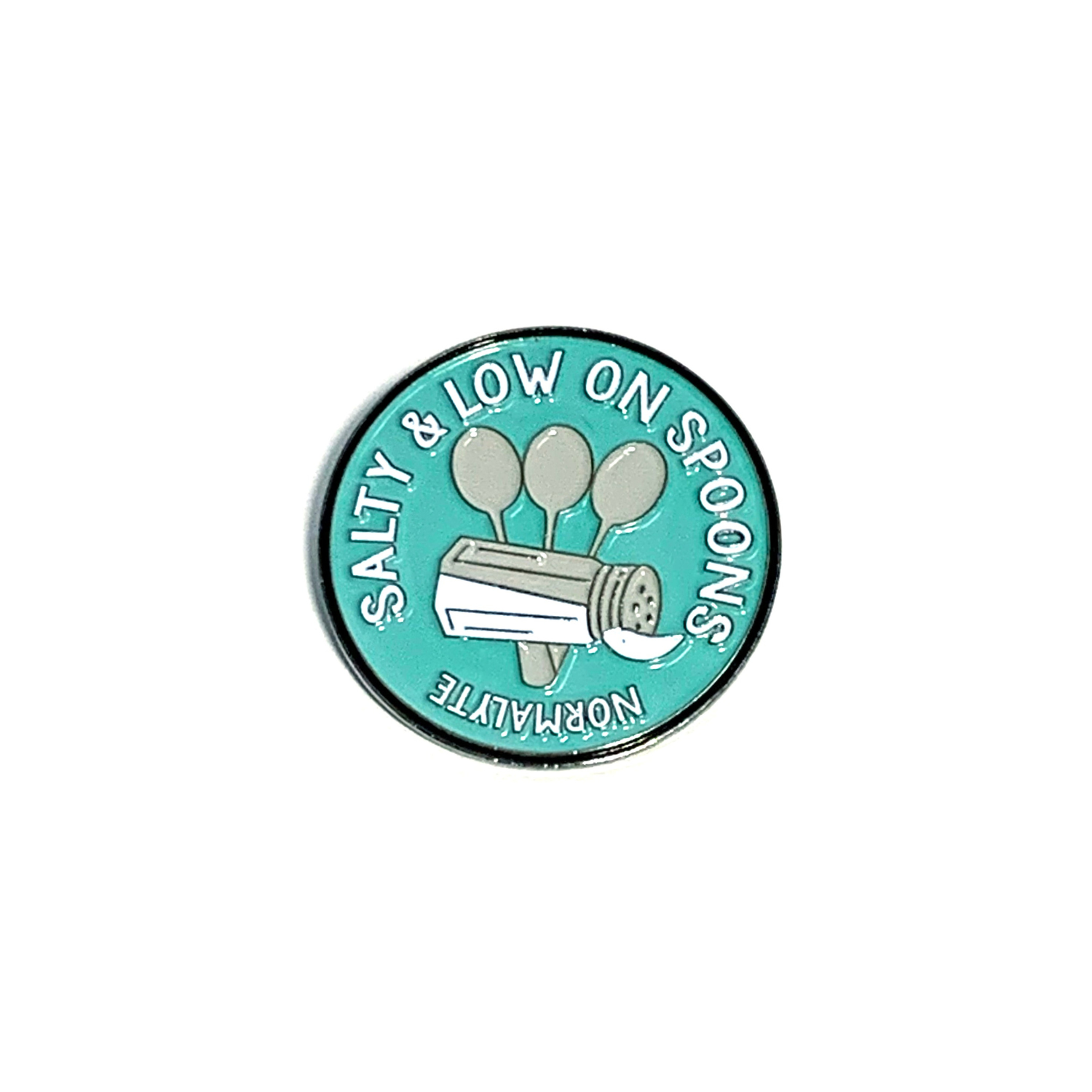 Round teal NormaLyte enamel lapel pin featuring a salt shaker pouring salt over three spoons, surrounded by the text "Salty & Low on Spoons"